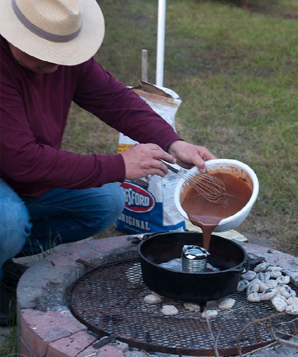 pouring cake batter into Dutch oven over outdoor fire
