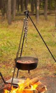 Meal cooking in a Dutch oven over a fire using a bale handle and tripod.