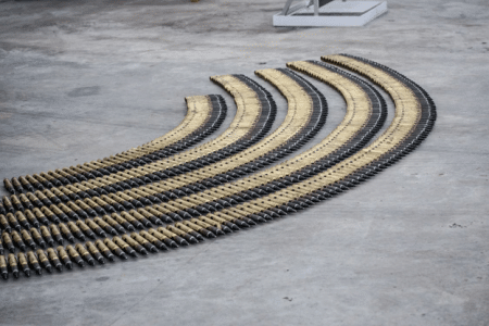 Curved rows of beige and black striped hoses laid on a gray concrete floor in a workshop setting.