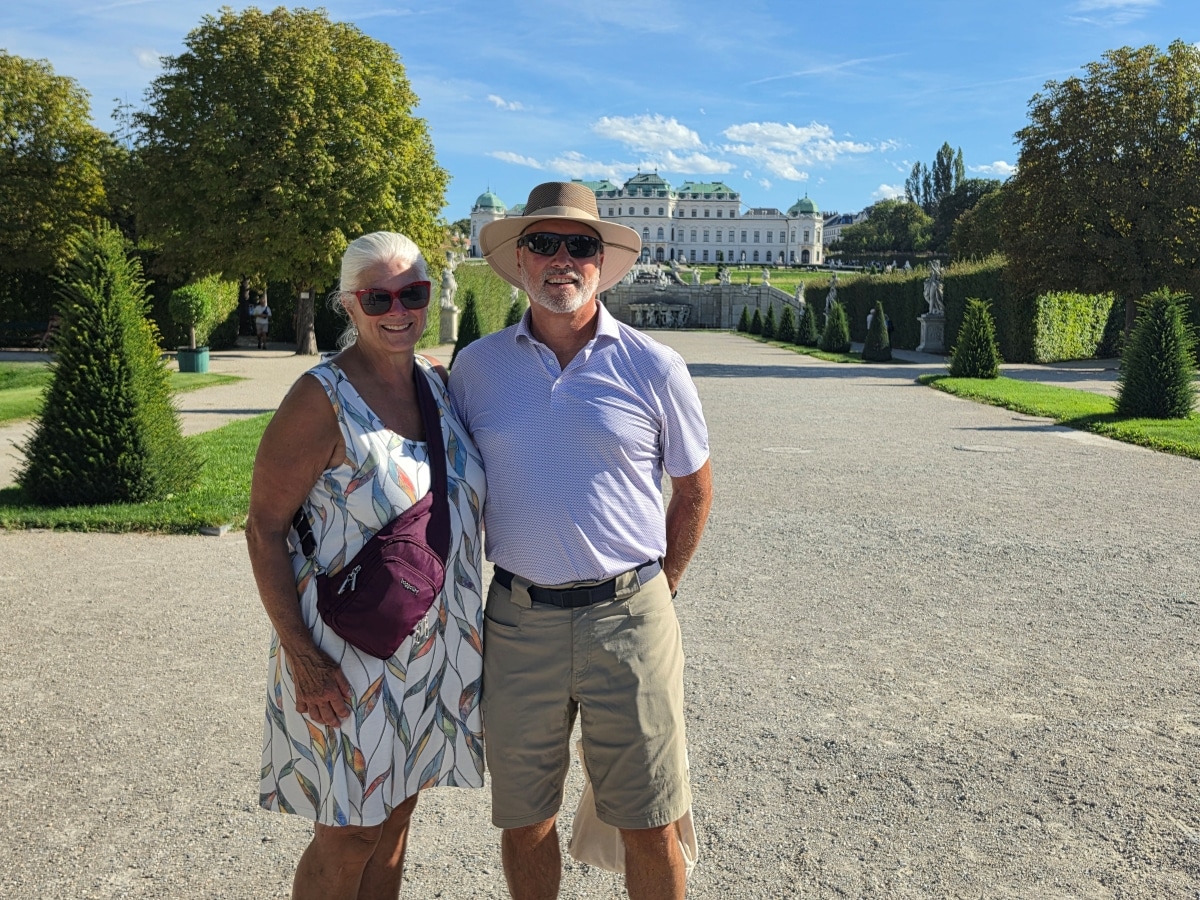 Couple posing in a formal garden with a grand white palace behind them on a sunny day